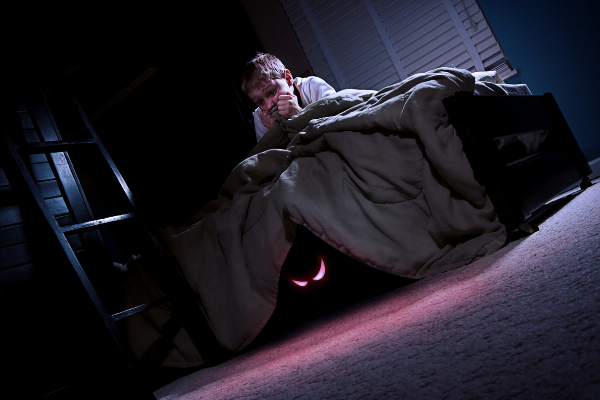 a scared kid in bed with glowing monster's eyes under the bed.