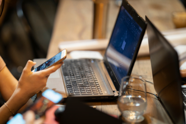 Woman using her smartphone and her laptop in cafe