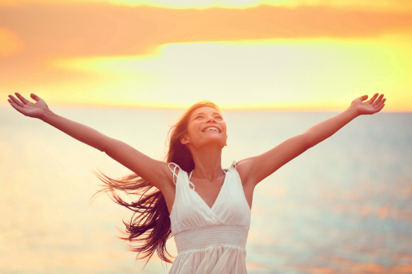 A smiling woman on the beach with her arms stretched wide.