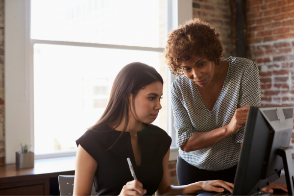 older woman mentoring a younger woman at her desk