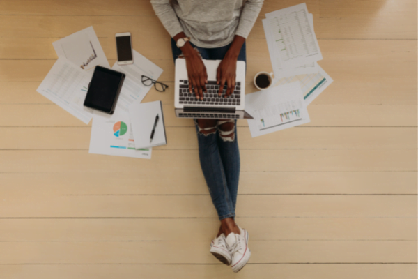 man sitting on the floor of his house with a laptop and work papers around him.